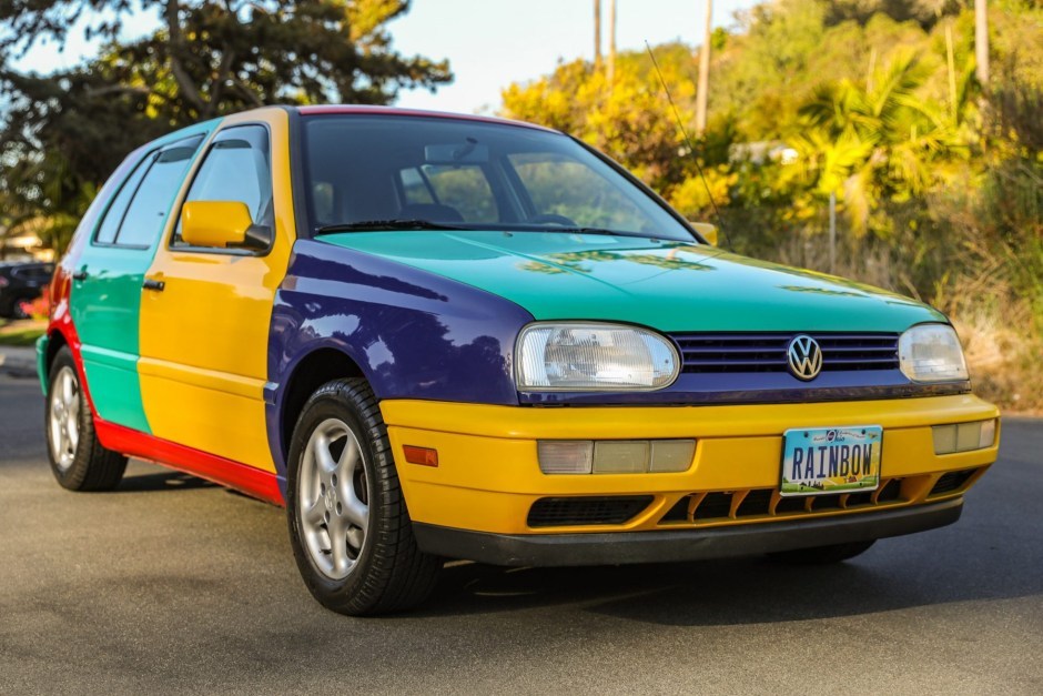 picture of a 1996 Volkswagen golf with a license plate that says "rainbow". it has a yellow front bumper and front door, teal hood, rear bumper and rear door, purple grill and front side panel, and red rocker panel, roof, and rear side panel.